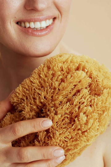 Nahaufnahme einer Frau mit großem Naturschwamm in der Hand – natürliche Hautpflege und sanftes Peeling