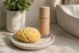 Kleiner Kosmetik-Naturschwamm neben Foundation und einer Keramikablage.