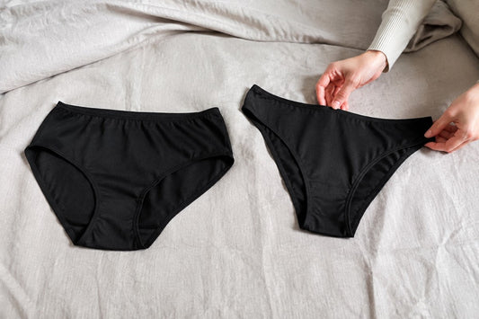 Zwei schwarze Slips mit unterschiedlichen Schnitten liegen auf hellem Stoff.