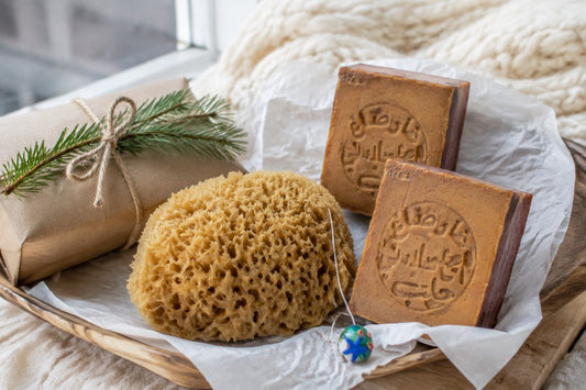 Naturschwamm mit Glasanhänger, zwei Aleppo-Seifen und ein schlichtes Geschenkpaket mit Tannenzweig.