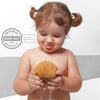 Kleinkind mit Zöpfen in der Badewanne drückt einen tropfnassen Babyschwamm aus Naturschwamm, Dermatest-Siegel sehr gut