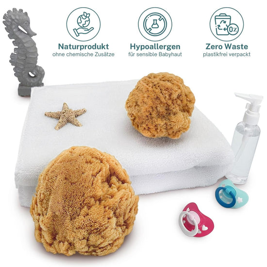 Zwei weiche Babyschwämme aus Naturschwamm auf weißem Handtuch mit Seestern, Schnullern und Lotionspender – Naturprodukt, hypoallergen, Zero Waste