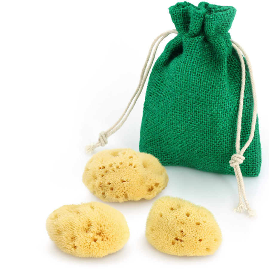 Drei gelbe Kosmetikschwämme aus Naturschwamm mit grünem Jute-Beutel auf weißem Hintergrund