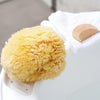Naturschwamm Grass auf dem Rand der Badewanne neben einem Holzkamm auf weißem Handtuch