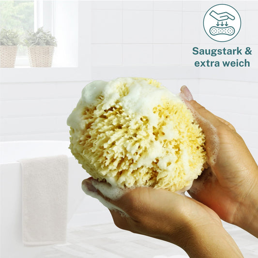 Hände halten in der Dusche einen schäumenden Naturschwamm Grass mit dem Hinweis saugstark und extra weich