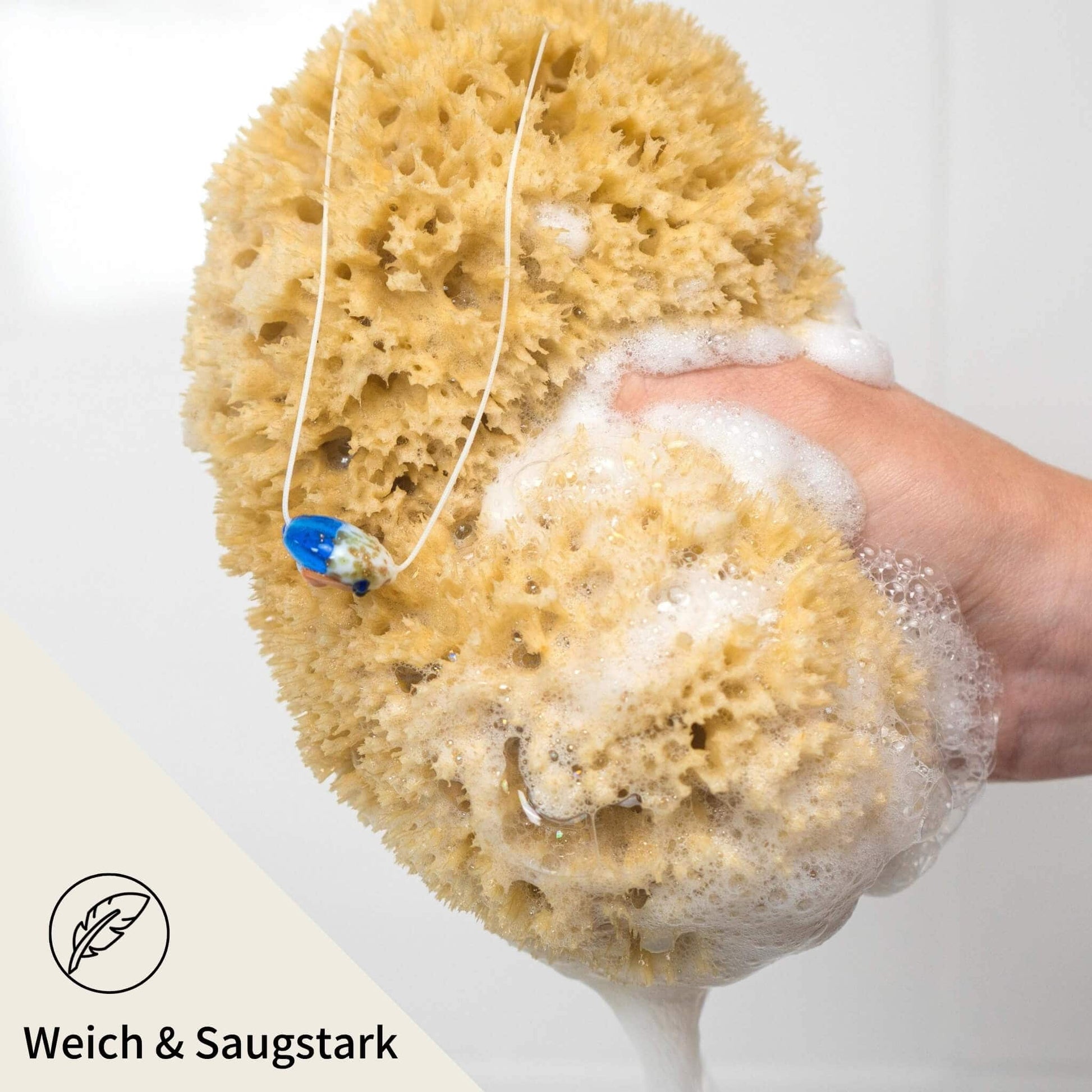 Hand hält schäumenden Naturschwamm mit Kordel – weich, saugstark und ideal zur täglichen Duschpflege